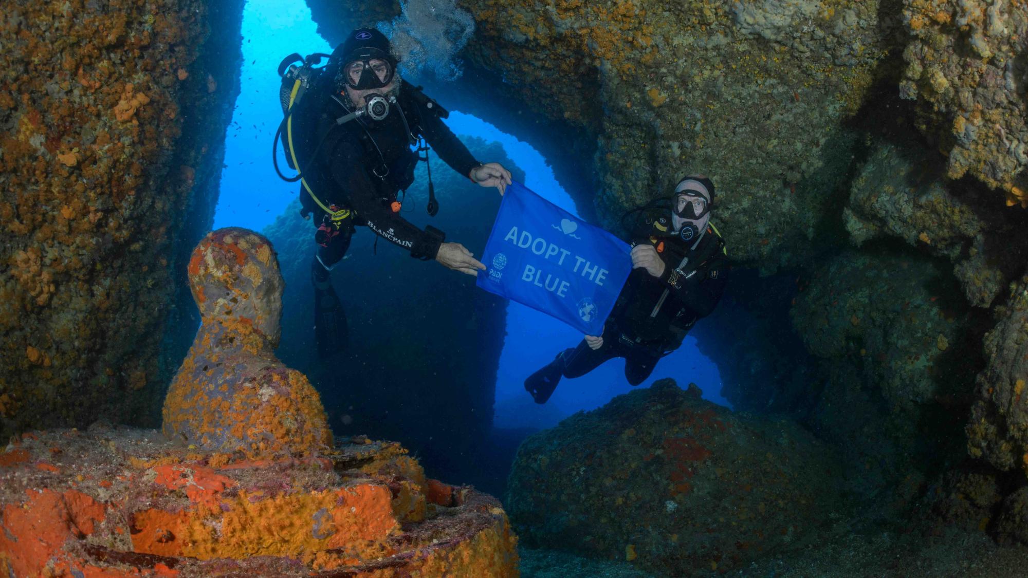 Divers holding a blue Adopt the Blue flag in the ocean.
